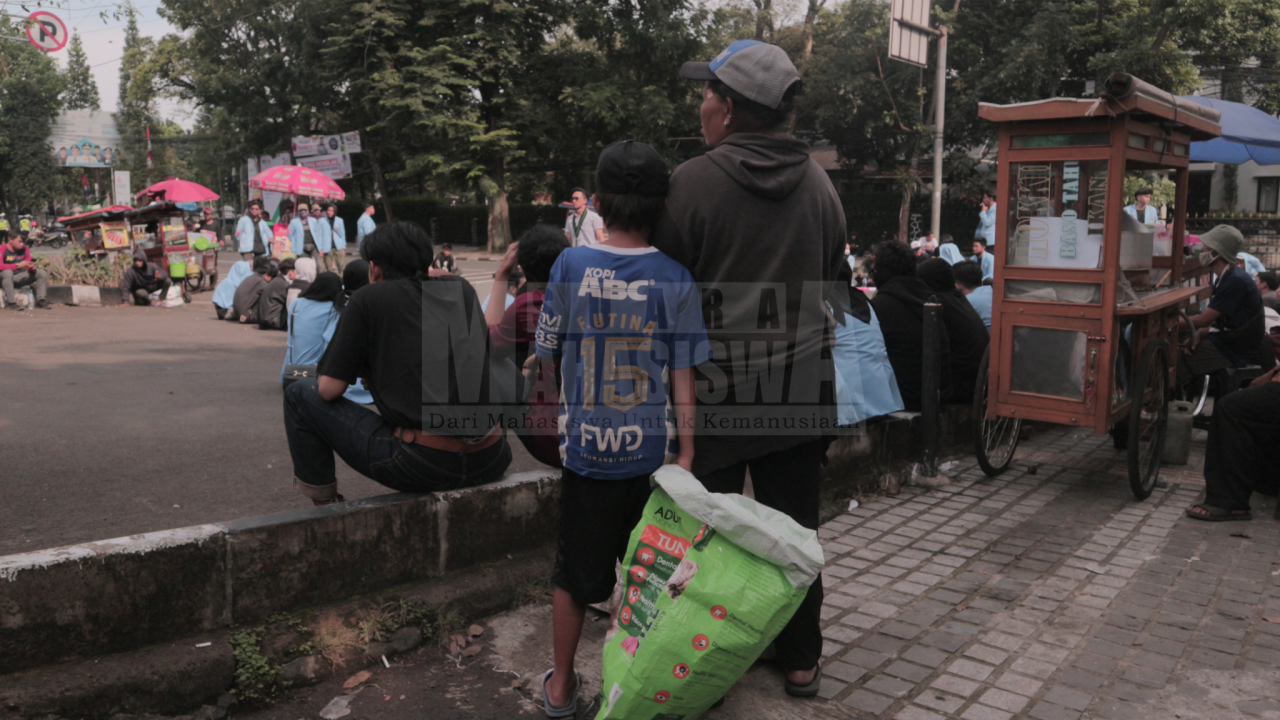 Foto seorang wanita paruh baya bersama anaknya yang sedang memegang karung berisi botol plastik bekas di tengah kerumunan massa aksi tolak kenaikan BBM di depan gedung Dewan Perwakilan Rakyat Daerah (DPRD) Jawa Barat, pada Selasa (13/9). (Foto: Tsabit Aqdam Fidzikrillah/SM)